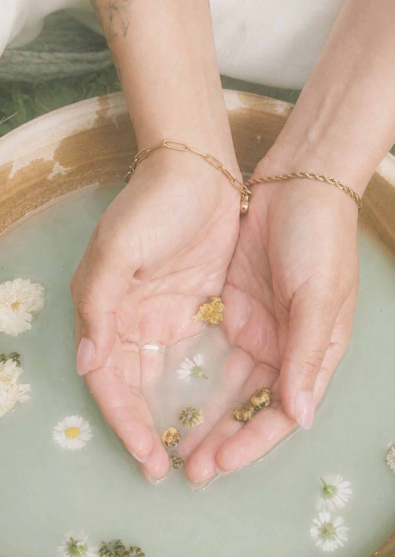 Hands cupping water with floating flowers in a milk bath